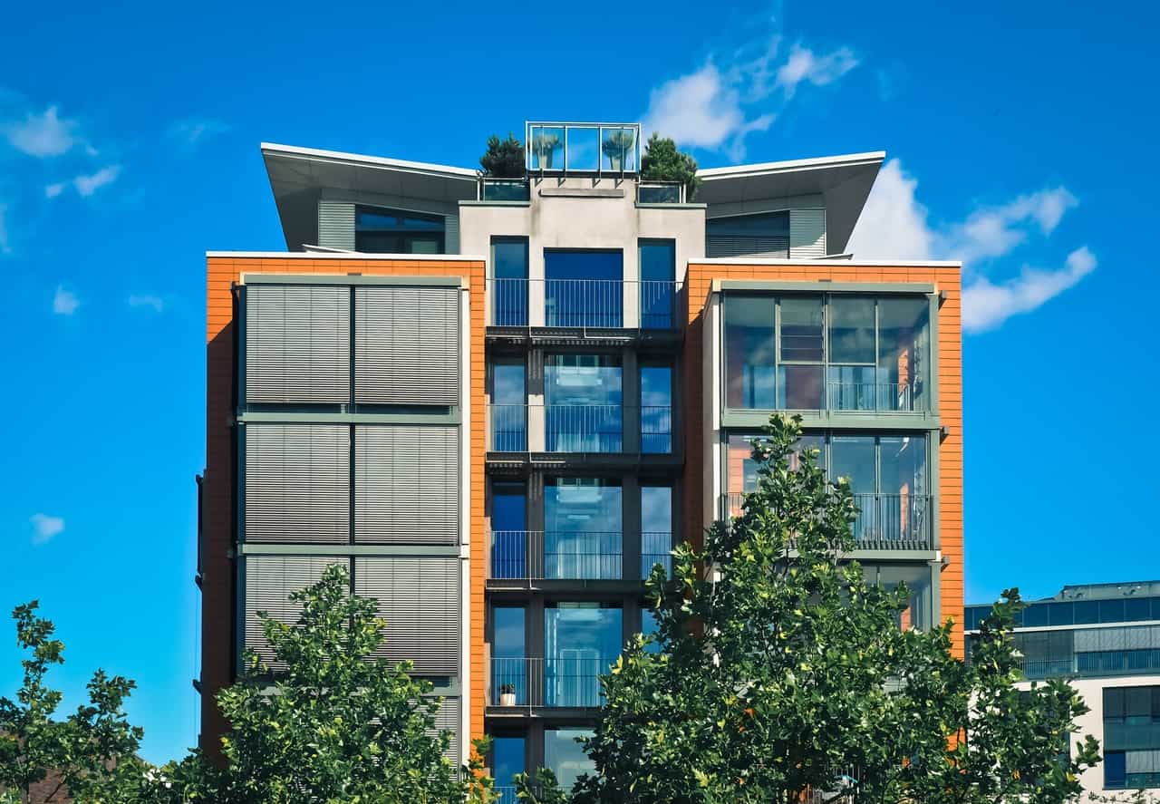 A modern mid-rise apartment building with glass balconies behind trees
