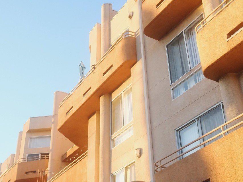 Ground-up angle of an apartment building with a tan exterior.. A sunlit stucco apartment building with balconies