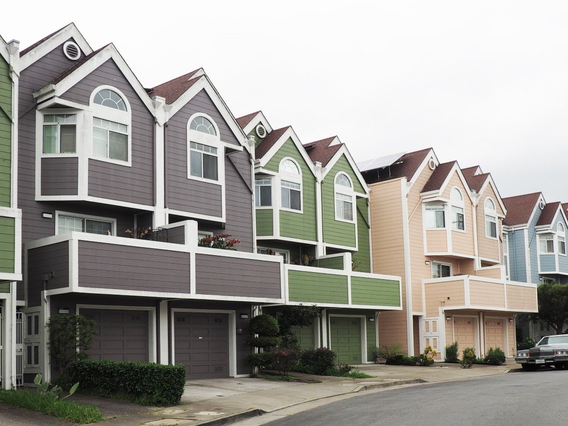 A row of pastel townhomes with tuck-under garages on a hillside street